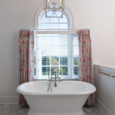 Free-standing bathtub in front of a window with red curtains.