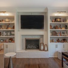 White fireplace with floor-to-ceiling open air shelves on either side. Hardwood floors and furniture to each side of the room.