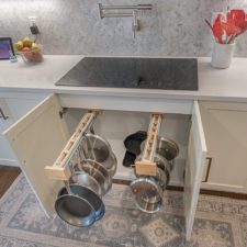 Pan hanging storage in cabinet below stovetop on counter